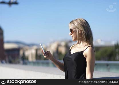 Side view of a blond girl checking a smart phone on the street