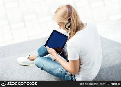 Side view of a happy young woman, listening to the music in vintage music headphones, surfing internet on a tablet pc and sitting on stairs against urban city background.
