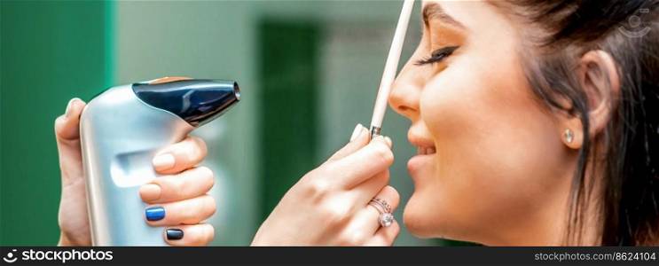 Side view of a make-up artist using aerograph making an airbrush makeup foundation on a female face in a beauty salon. Side view of a make-up artist using aerograph making an airbrush makeup foundation on a female face in a beauty salon.