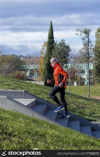 Side view of a senior caucasian athlete man training running up and down the stairs outdoors in a park in a sunny day