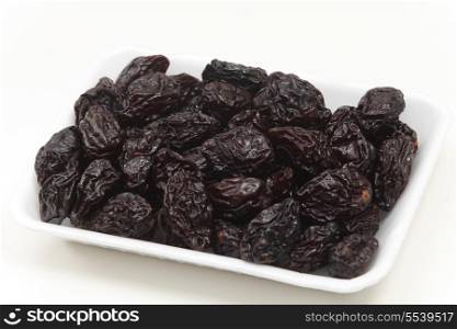 Side view of a supermarket tray of prunes over a white background.