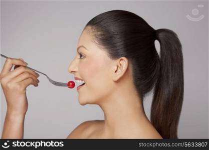 Side view of a woman eating cherry tomato on fork