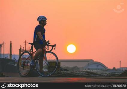 Side view of adult athletic man on bike is taking break and relaxing at harbor after long distance workout in sunset time