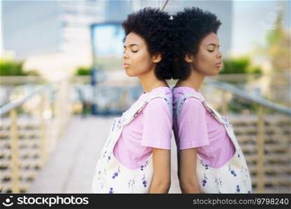 Side view of African American female with closed eyes standing near glass building on street of city against blurred background. Calm black woman near glass house