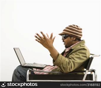 Side view of African-American mid-adult man wearing hat and making surprised expression at laptop computer.