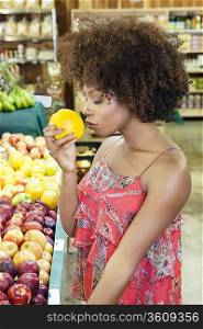Side view of African American woman smelling fresh orange at supermarket