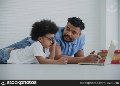 Side view of African father looking at little boy wear glasses rubbing his eyes because of pain and dry in eyes while using laptop computer for learning class online at home