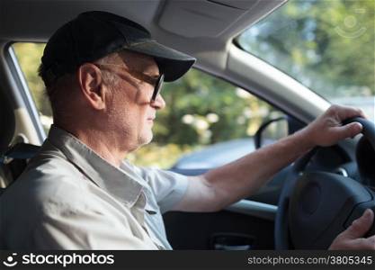 Side view of an elderly man in glasses driving a car on a sunny summer day