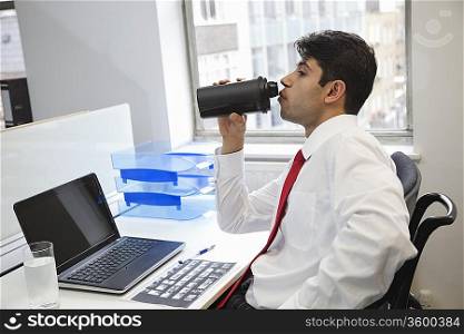 Side view of an Indian businessman drinking water at office desk