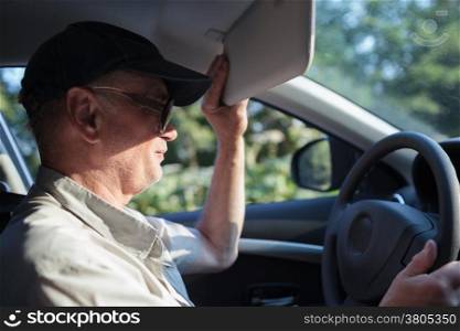 Side view of an old man at the wheel trying to hide himself from the sun with a sun visor