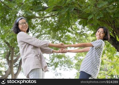Side view of Asian mother and daughter holding hand and smile while standing in the park, Happy family concept