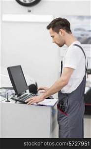 Side view of automobile mechanic using computer in workshop