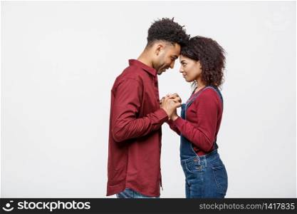 Side view of beautiful African American young couple in classic shirts holding hands, looking at each other and smiling. Side view of beautiful African American young couple in classic shirts holding hands, looking at each other and smiling.