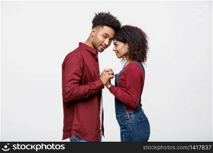 Side view of beautiful African American young couple in classic shirts holding hands, looking at each other and smiling. Side view of beautiful African American young couple in classic shirts holding hands, looking at each other and smiling.