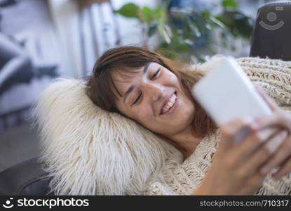 side view of beautiful young smiling woman lying on leather couch relaxing while using a mobile phone at home. Rafa Fernandez