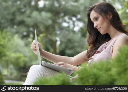 Side view of beautiful young woman using laptop in park