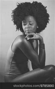 Side view of black woman in bodysuit with Afro hairstyle touching chin and looking away over shoulder while sitting under. Black and white photograph.. Black and white photograph of an African American model under neon illumination