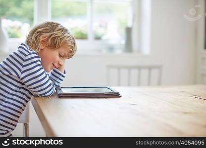 Side view of boy sitting at table, using digital tablet