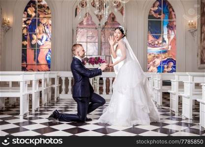 Side view of bridegroom putting ring on surprised bride’s finger in church
