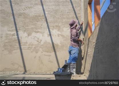 Side view of builder worker using long trowel to polishing cement wall inside of house construction site