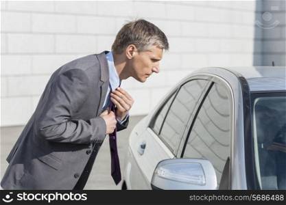 Side view of businessman adjusting tie while looking in car window