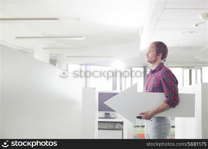 Side view of businessman holding arrow sign in creative office