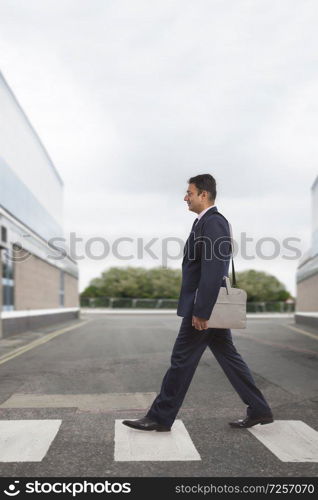 Side view of businessman in formal clothes carrying office bag crossing the street on zebra crossing