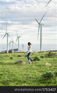 Side view of carefree female running in field with windmills and playing with adorable dog while enjoying summer weekend on Lanzarote. Woman playing with dog in meadow with windmills