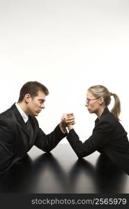 Side view of Caucasian mid-adult businessman and businesswoman arm wrestling on table.