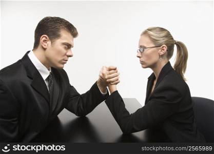 Side view of Caucasian mid-adult businessman and businesswoman arm wrestling on table.