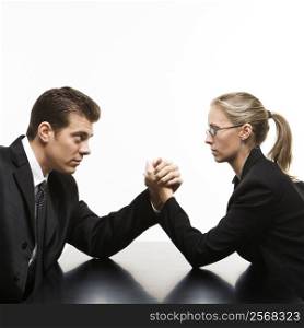 Side view of Caucasian mid-adult businessman and businesswoman arm wrestling on table.