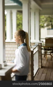 Side view of Caucasian pre-teen girl standing on porch.