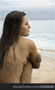 Side view of Caucasian young adult nude woman sitting on beach.