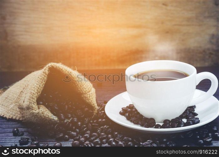 Side view of Coffee cup with smoke and coffee beans in sack on wood table, Drinks and relax concept, for advertising