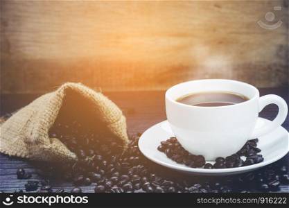 Side view of Coffee cup with smoke and coffee beans in sack on wood table, Drinks and relax concept, for advertising