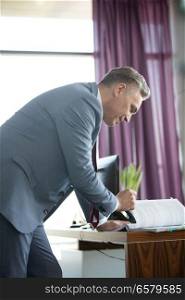 Side view of confident mature businessman reading book at desk in office