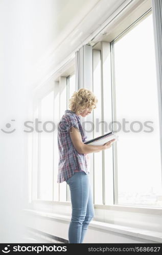 Side view of creative businesswoman reading file by window in office
