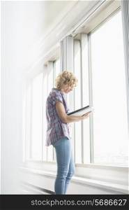 Side view of creative businesswoman reading file by window in office