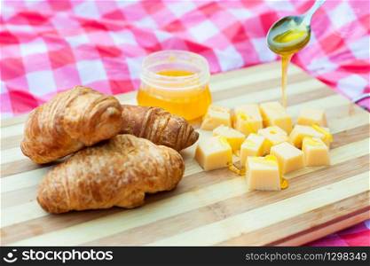 Side view of different products on the blanket served for picnic: cheese, honey and croissants. Food for picnic