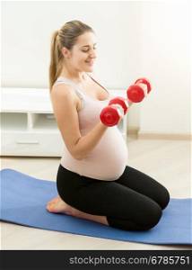 Side view of expectant mother exercising with dumbbells on fitness mat