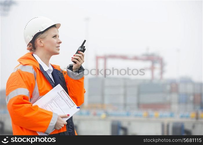 Side view of female engineer using walkie-talkie in shipping yard