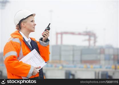 Side view of female engineer using walkie-talkie in shipping yard