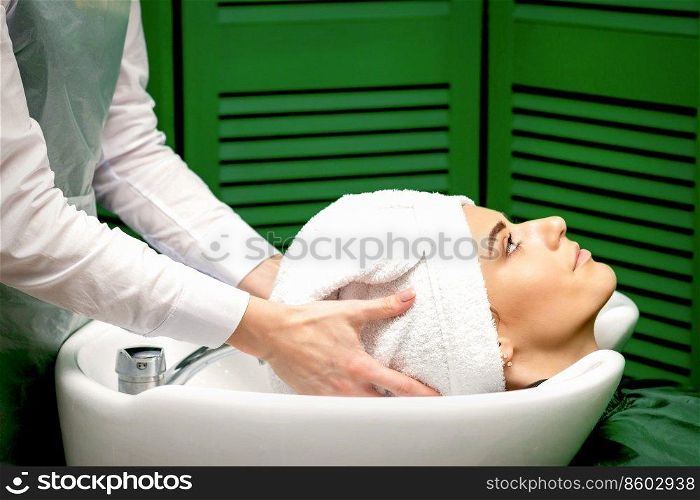 Side view of female hairdresser dries the female client&rsquo;s hair with a towel in the sink at a hair salon. Hairdresser dries the client&rsquo;s hair