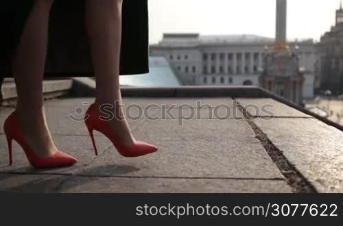 Side view of female slender legs in high heels going down the stone stairs in the city. Elegant woman wearing mini skirt and emerald green coat stepping down on stairway. Closeup of beautiful slim legs walking down staircase. Slow motion.