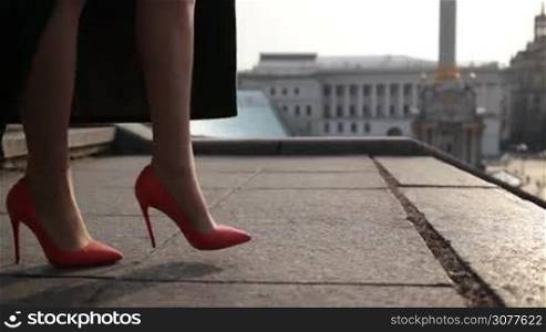 Side view of female slender legs in high heels going down the stone stairs in the city. Elegant woman wearing mini skirt and emerald green coat stepping down on stairway. Closeup of beautiful slim legs walking down staircase. Slow motion.