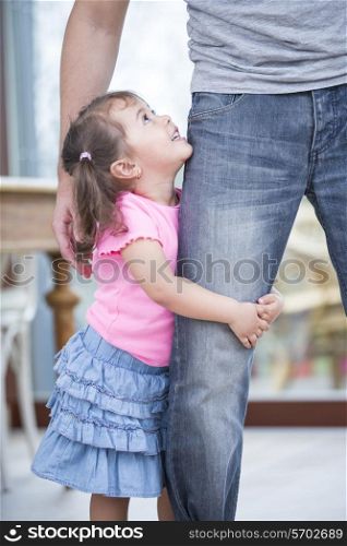 Side view of girl hugging father&rsquo;s leg in house