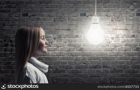 Side view of girl of school age looking at hanging bulb