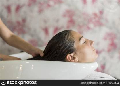 Side view of Hairdresser hands washing hair of a beautiful woman in hair salon.