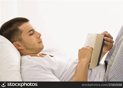 Side view of handsome Caucasian mid adult man lying in bed reading a book.