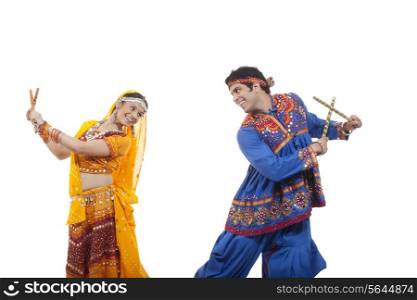 Side view of happy couple in traditional wear looking at each other while performing Dandiya Raas against white background